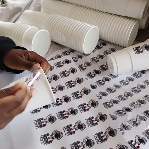 Image shows Vinyl Stickers being applied to evet drinking cups by BrandXellence - stickers are on vinyl stickers sheets vinyl stickers printing